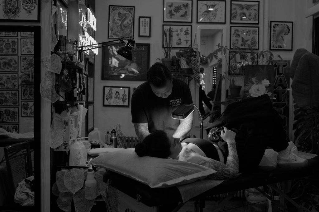 Mike Stapleton tattooing a client lying on the table in a studio lined with flash
